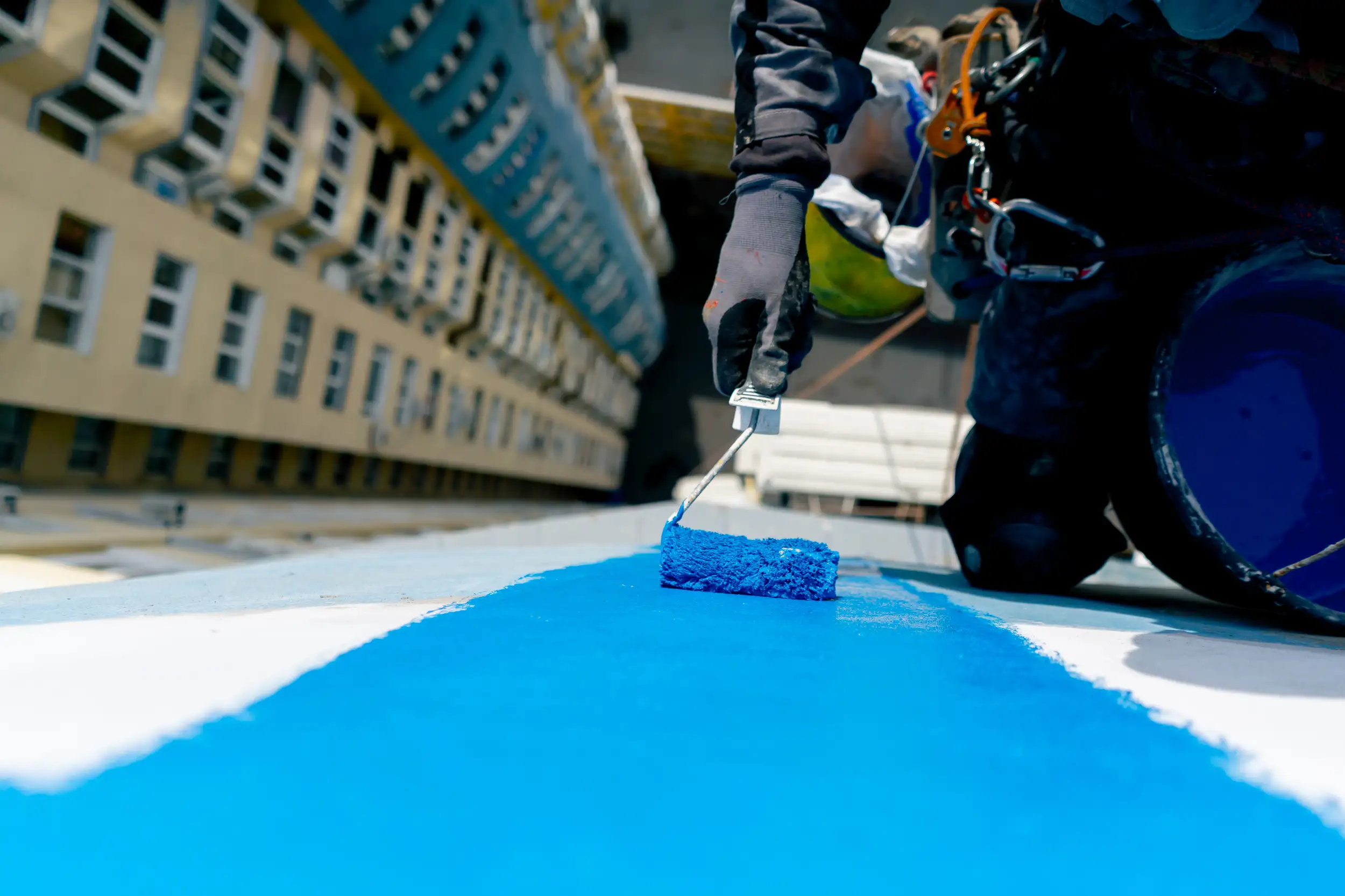 A paint service worker painting at the top of the building.