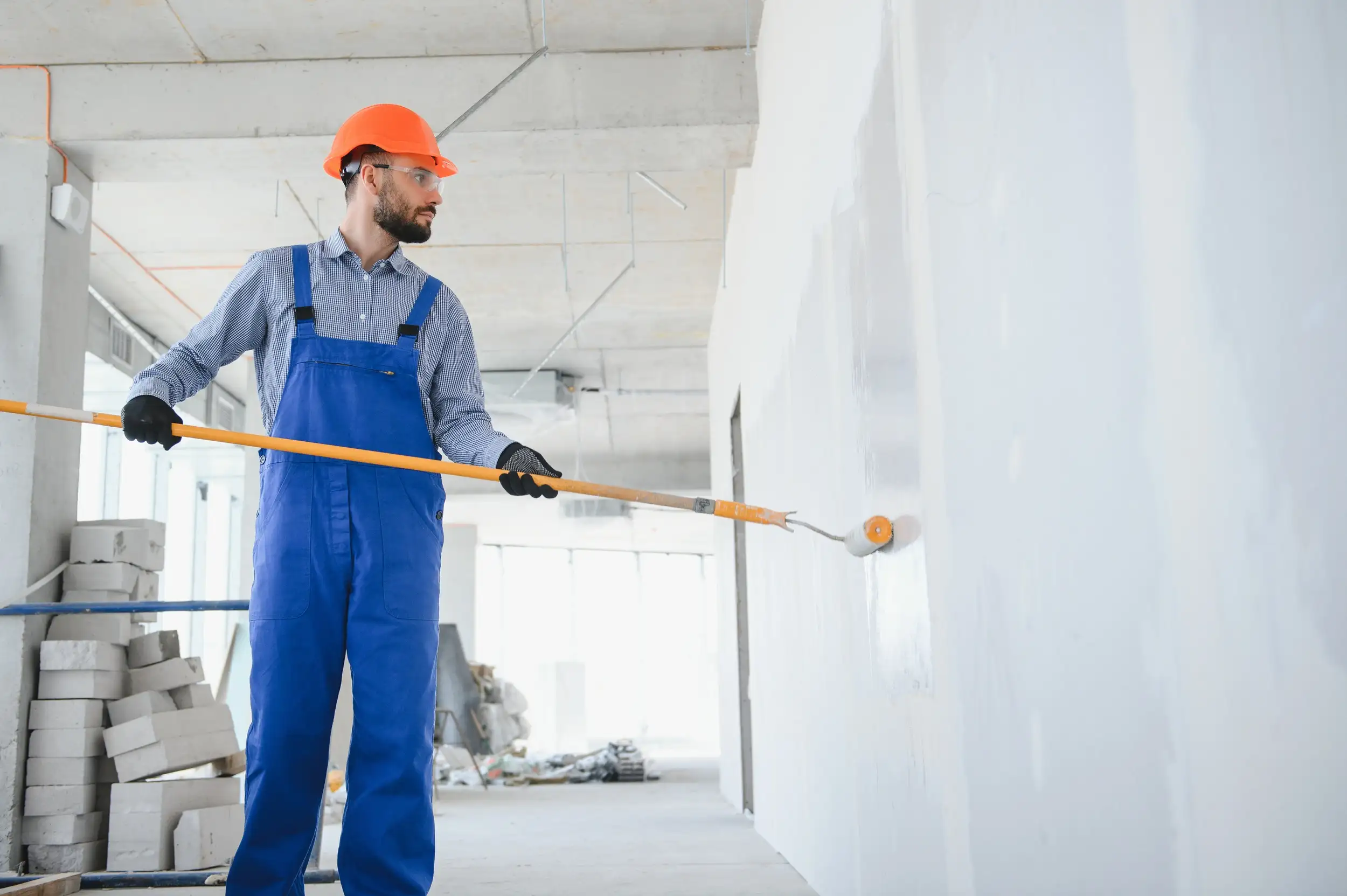 A man with hard helmet painting the walls with white color.